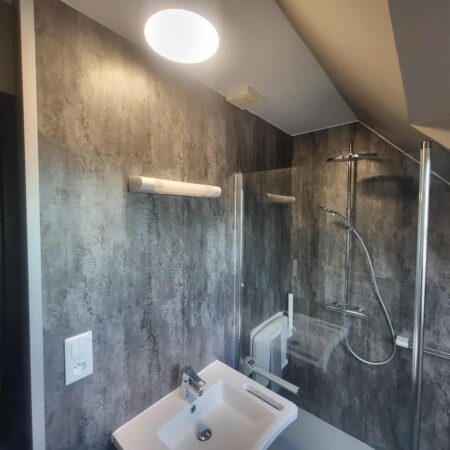 transformation complète de salle de bain à Aulnoy Lez Valenciennes, nouveau WC et un lavabo moderne, posé du placo hydrofuge, des panneaux muraux aspect béton clair mat et un revêtement de sol PVC facile d’entretien.