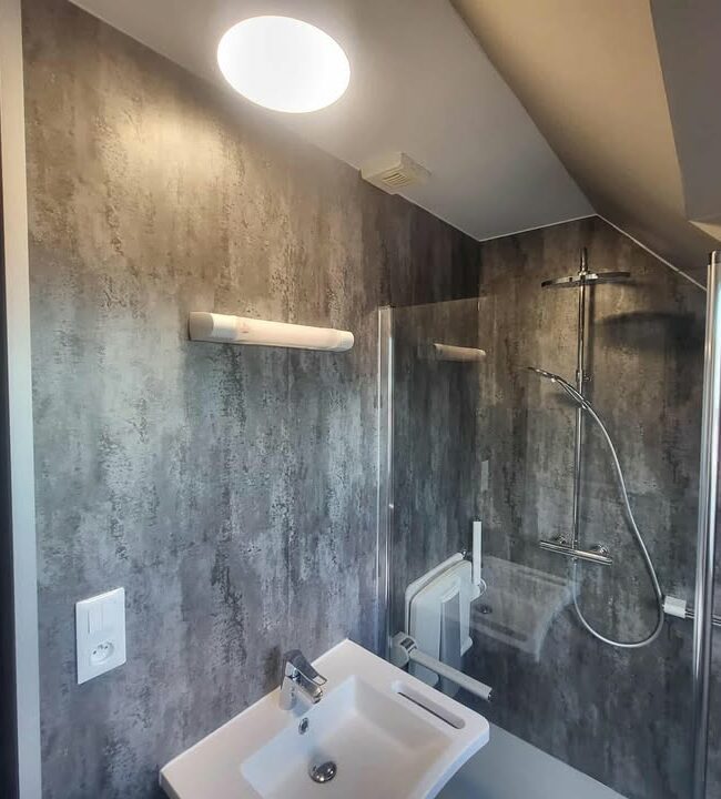 transformation complète de salle de bain à Aulnoy Lez Valenciennes, nouveau WC et un lavabo moderne, posé du placo hydrofuge, des panneaux muraux aspect béton clair mat et un revêtement de sol PVC facile d’entretien.