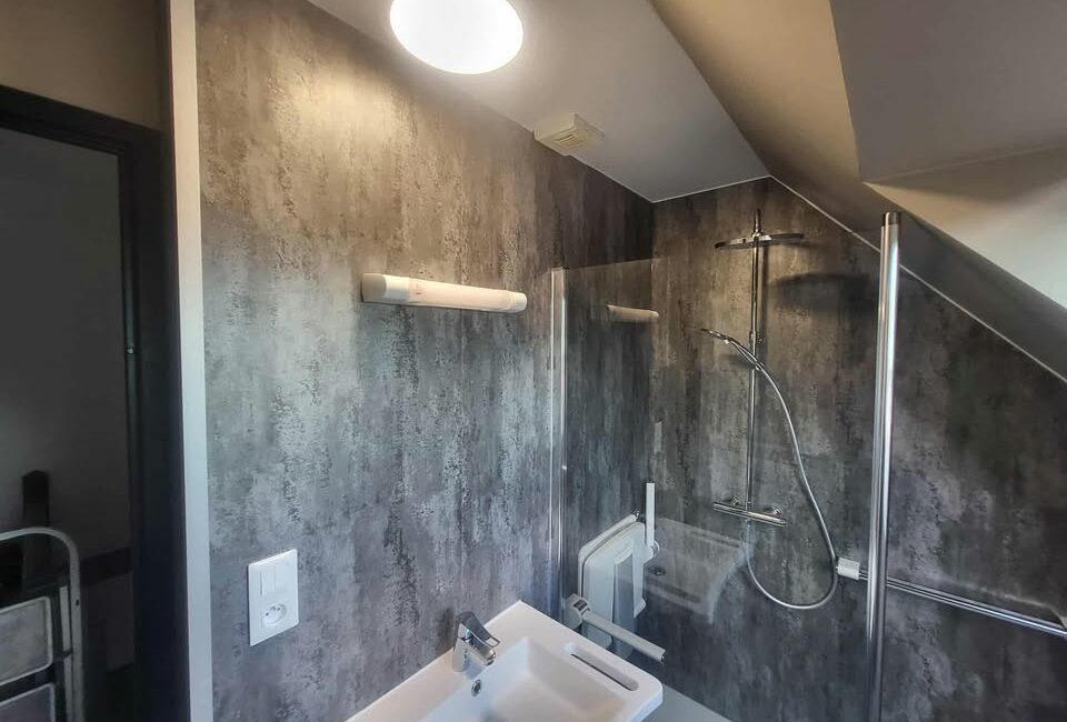 transformation complète de salle de bain à Aulnoy Lez Valenciennes, nouveau WC et un lavabo moderne, posé du placo hydrofuge, des panneaux muraux aspect béton clair mat et un revêtement de sol PVC facile d’entretien.